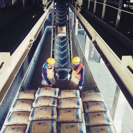 Workers stacking cement bags on a conveyor in a plant